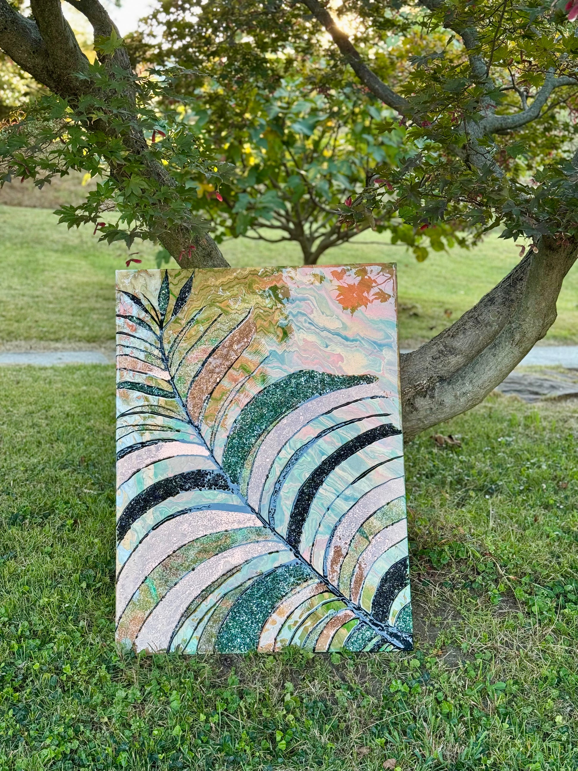 Colorful abstract leaf painting and resin art on grass with trees in the background