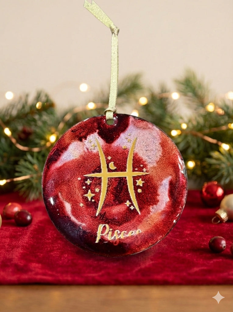 Decorative Pisces zodiac ornament on a red fabric with Christmas lights and decorations in the background.