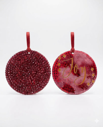Two red glittery Christmas ornaments with 'Joy' text on a white background